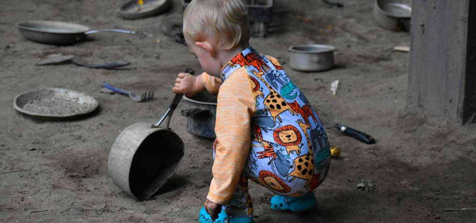 child crouched in mud cafe playing with a pot