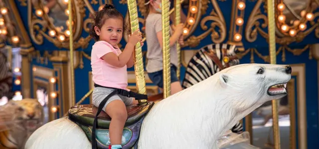 A little girl riding a polar bear on a carousel.